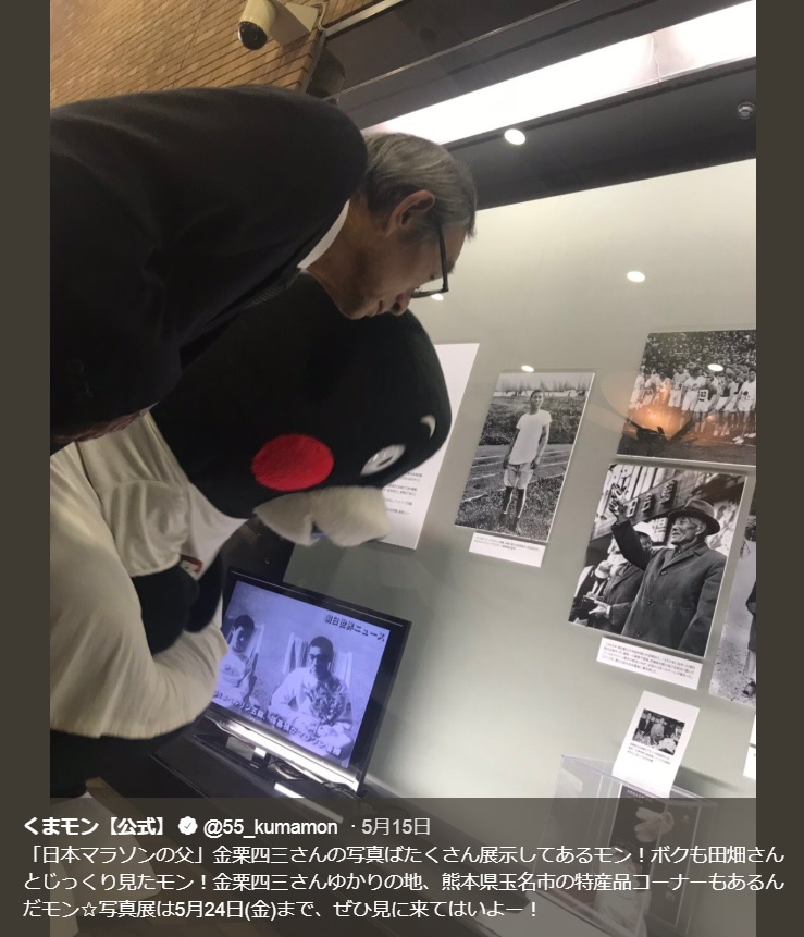 田畑政治さんの写真に見入る田畑和宏さんとくまモン（画像は『くまモン【公式】　2019年5月15日付Twitter「「日本マラソンの父」金栗四三さんの写真ばたくさん展示してあるモン！」』のスクリーンショット）