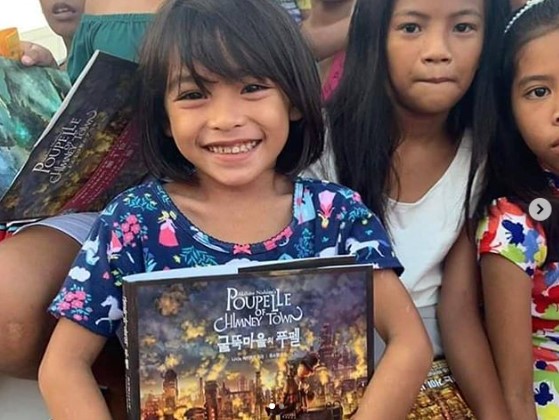 かつての支援で西野の絵本を手にした子供たち（画像は『AKIHIRO NISHINO　2019年9月20日付Instagram「グラミー賞を6度受賞されている『ブラックアイドピーズ』のアップルさんと一緒に、フィリピンの子供達にクリスマスプレゼントを贈ることになりました。」』のスクリーンショット）