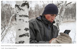 外の寒さの中でネット回線を確認するアレクセイさん（画像は『PRI.org　2020年11月19日付「Siberian student scales birch tree for internet access as classes move online」（Credit: Alexey Malgavko/Reuters）』のスクリーンショット）