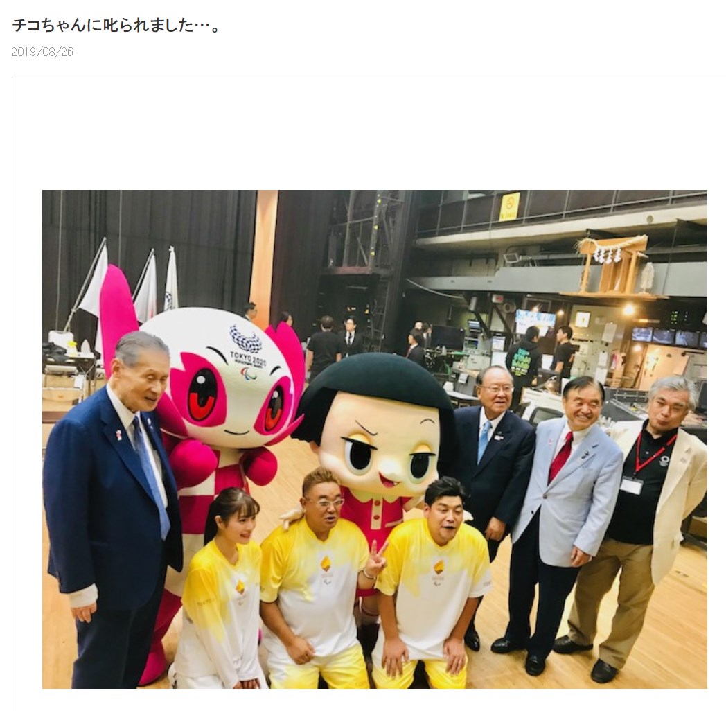 東京2020オリンピック・パラリンピック競技大会組織委員会の森喜朗会長（左）やチコちゃんと記念写真に納る聖火リレー公式アンバサダーたち（画像は『サンドウィッチマン 伊達みきお　2019年8月26日付オフィシャルブログ「チコちゃんに叱られました…。」』のスクリーンショット）