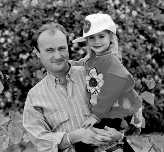 父フィル・コリンズに抱かれる幼少時のリリー（画像は『Lily Collins　2021年1月30日付Instagram「Happy 70th birthday dad!!」』のスクリーンショット）