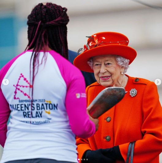 カディーナ・コックス選手にバトンを手渡すエリザベス女王（画像は『The Royal Family　2021年10月7日付Instagram「The Queen signing her message to the Commonwealth, which will be read at the Opening Ceremony of the Commonwealth Games in Birmingham next year.」』のスクリーンショット）