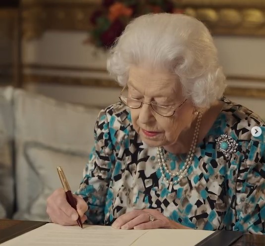 バトンに入れる手紙に署名する女王（画像は『The Royal Family　2021年10月7日付Instagram「The Queen signing her message to the Commonwealth, which will be read at the Opening Ceremony of the Commonwealth Games in Birmingham next year.」』のスクリーンショット）