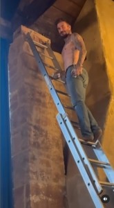 天井近くまである梯子を登り、カメラの方を振り向くデヴィッド。ジーンズとソックス姿で、上半身は裸だ（『Victoria Beckham　Instagram「The electrician is back!!!」』より）